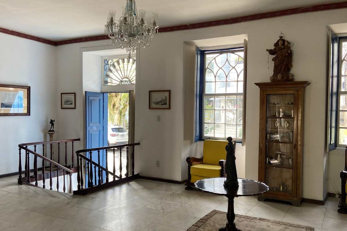 Hall histórico com escada, cristaleira e janelas coloniais azuis